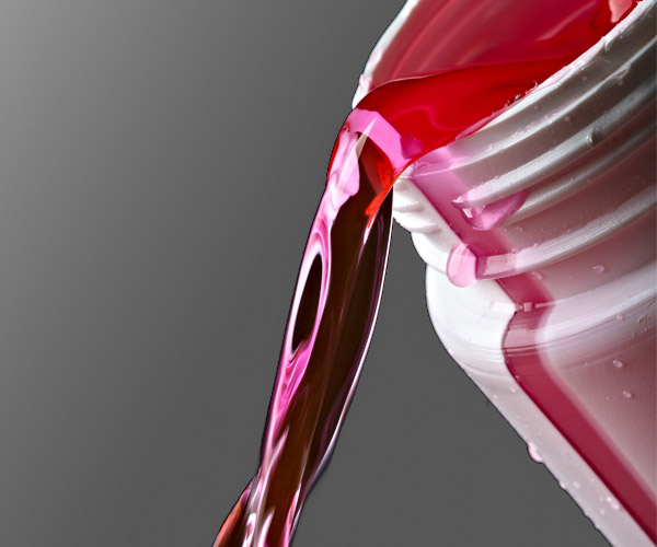 Close up image of pouring pink antifreeze out of white bottle.