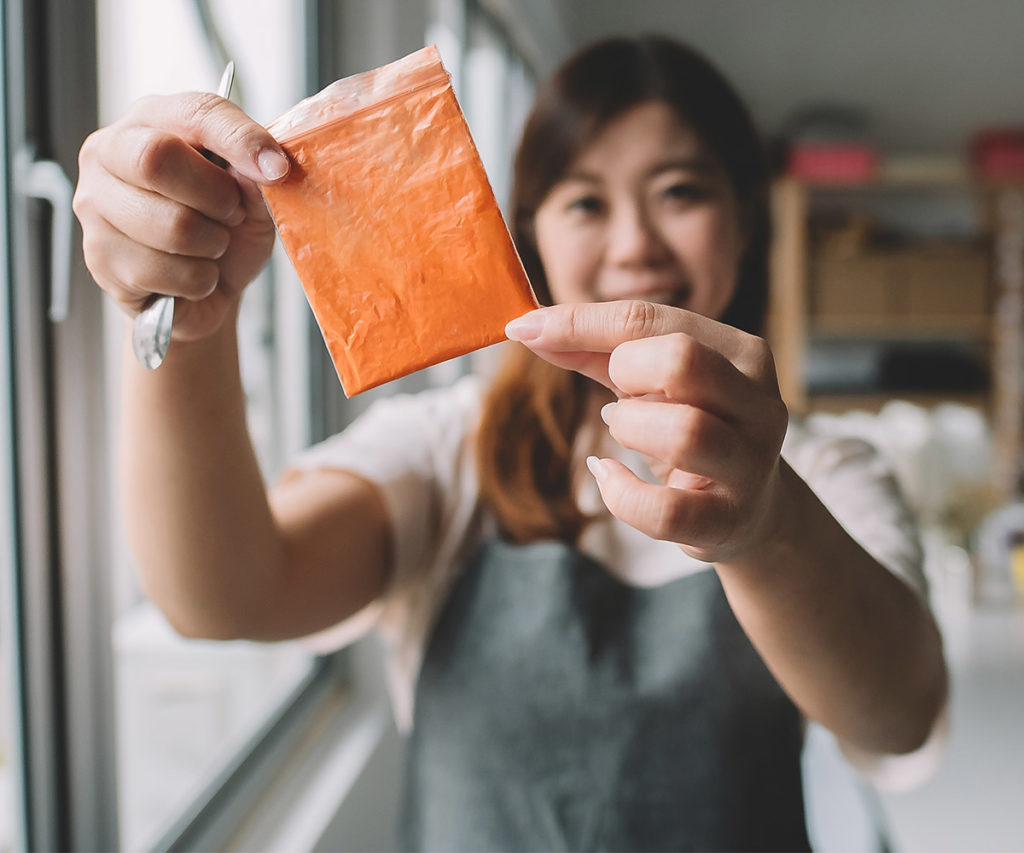 Woman holding up small packet of orange powered dye.