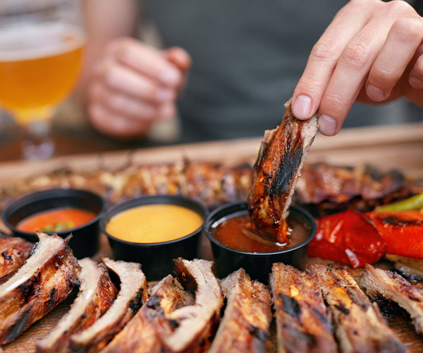 A woman dips baby back rib into barbecue sauce.