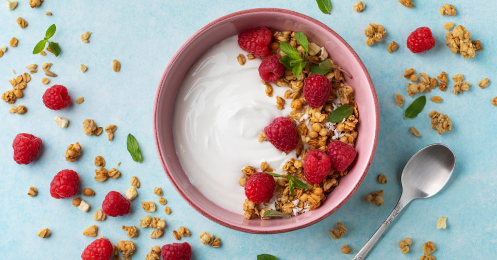 A delicious bowl of yogurt topped with fresh raspberries and granola. 